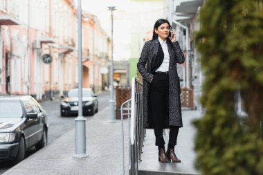Şehirdeki çekici genç kadın. İş kadını, modern iş merkezinin önünde akıllı bir telefonla konuşurken gülümsüyor.