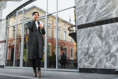 Şehirdeki çekici genç kadın. İş kadını, modern iş merkezinin önünde akıllı bir telefonla konuşurken gülümsüyor.