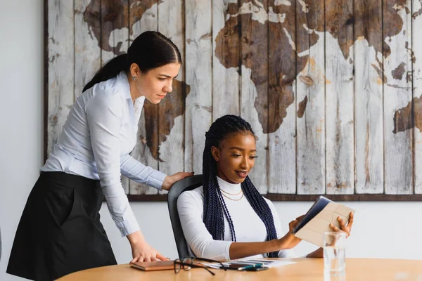 Ofiste çalışan iki çekici genç kadın bir dizüstü bilgisayarı paylaşıp ekranda bilgi okurken tartışıyorlar.