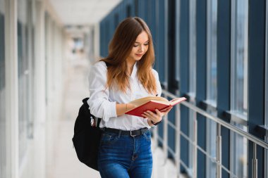 Siyah sırt çantalı neşeli esmer kız öğrenci modern binada kitapları tutuyor. Üniversite koridorunda elinde kitaplarla duran kız öğrenci.