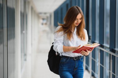 Üniversite koridorunda elinde kitap ve sırt çantası olan güzel bir kız öğrencinin portresi.