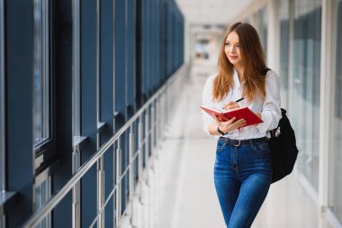Pozitif, güzel bir kız kameraya gülümsüyor, koridorda sırt çantası gibi notlarla duruyor, derse gidiyor. Lüks üniversitede okuyan mutlu esmer kız öğrenci..