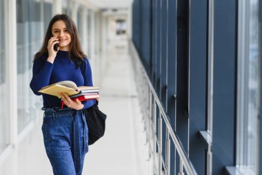 Üniversite koridorunda elinde kitap ve sırt çantası olan güzel bir kız öğrencinin portresi.