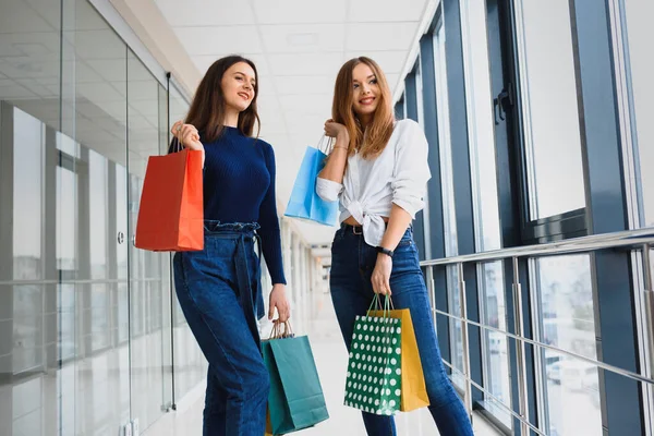 モールセンターでは幸せな2人の白人女性が一緒に買い物をしています 2人の若い女性がモールで買い物袋を持って歩いている — ストック写真