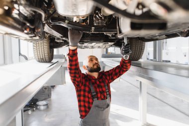 Tamirhanede arabanın altında çalışan tamirci. Otomobil tamircisi garajda çalışıyor. Onarım servisi.