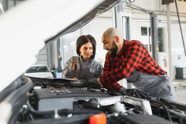 Auto car repair service center. Mechanic examining car engine. Female Mechanic working in her workshop. Auto Service Business Concept. Pro Car female Mechanic Taking Care of Vehicle.