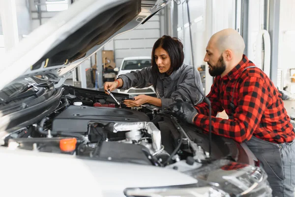 Auto car repair service center. Mechanic examining car engine. Female Mechanic working in her workshop. Auto Service Business Concept. Pro Car female Mechanic Taking Care of Vehicle.