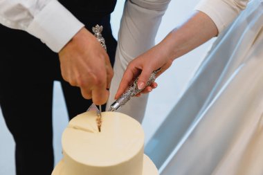 Gelin ve damadın elleri bir dilim düğün pastasından kesilmiş.