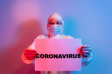 Coronavirus ve karantina konsepti. Koruyucu takım elbiseli, gözlüklü ve yüz maskeli profesyonel bir doktor. Önde el ele tutuşuyor, mavi arka planda tek başına duruyor.