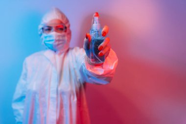 Koruyucu giysili, laboratuvar önlüklü, koruyucu gözlüklü ve maskeli kadın doktor antibakteriyel spreyle ayakta duruyor. Koronavirüsü durdurun. COVID-19.