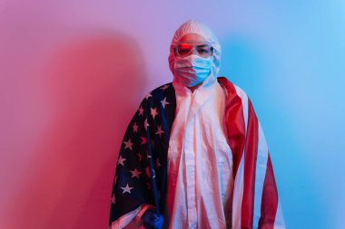 Birleşik Devletler 'i koronavirüs salgınından kurtar. COVID 19 koruyucu giysili doktor, maske ve eldivenli Amerikan bayrağı. Karantina konsepti.