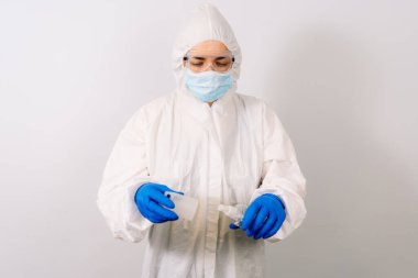 Mikrop ve virüslere karşı el dezenfektanı. Alkol içeriyor. Mavi eldiven giyen bir doktor elinde bir şişe tutuyor. Arka planda bulanık bir doktor var. Koronavirüsü durdurun. COVID-19.