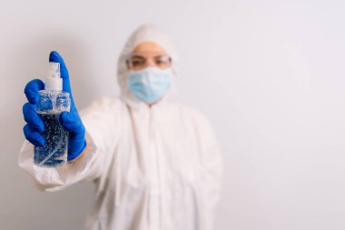 Mikrop ve virüslere karşı el dezenfektanı. Alkol içeriyor. Mavi eldiven giyen bir doktor elinde bir şişe tutuyor. Arka planda bulanık bir doktor var. Koronavirüsü durdurun. COVID-19.