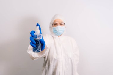 Mikrop ve virüslere karşı el dezenfektanı. Alkol içeriyor. Mavi eldiven giyen bir doktor elinde bir şişe tutuyor. Arka planda bulanık bir doktor var. Koronavirüsü durdurun. COVID-19.