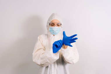 Koruyucu giysili ve solunum maskeli, eldivenli, kendine güvenen bir doktor. Mavi arka planda fotokopi aletiyle tek başına duruyor.