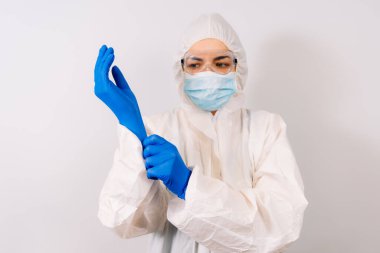 Koruyucu giysili ve solunum maskeli, eldivenli, kendine güvenen bir doktor. Mavi arka planda fotokopi aletiyle tek başına duruyor.
