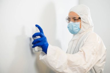 Koruyucu kıyafetli bir hemşire ya da doktor, şişeden beyaz el dezenfektanı. Alkol bazlı spreyli antibakteriyel jel. Coronavirus kontrol konsepti. Karantina.