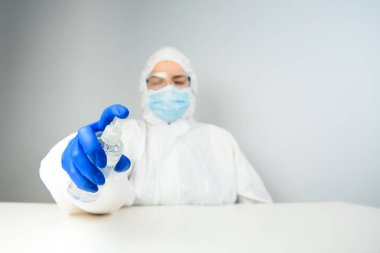 Koruyucu kıyafetli bir hemşire ya da doktor, şişeden beyaz el dezenfektanı. Alkol bazlı spreyli antibakteriyel jel. Coronavirus kontrol konsepti. Karantina.