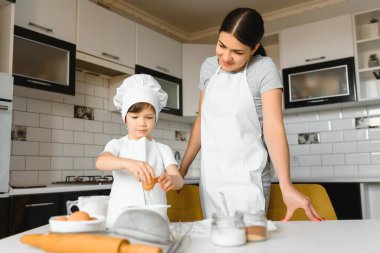 Happy mother and her little son shaking raw eggs in bowl before making dough for homemade pastry in the kitchen