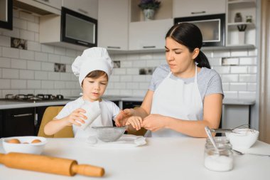 Genç ve güzel bir anne, küçük oğluyla birlikte mutfakta yemek hazırlıyor.