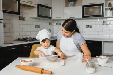 Genç ve güzel bir anne, küçük oğluyla birlikte mutfakta yemek hazırlıyor.