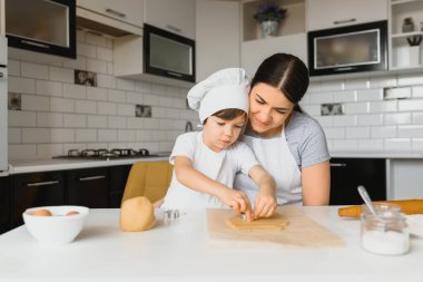Küçük çocuk, annesine mutfakta pişirmede yardım ediyor tezgahın yanında duruyor ve pastayı yoğuruyor.