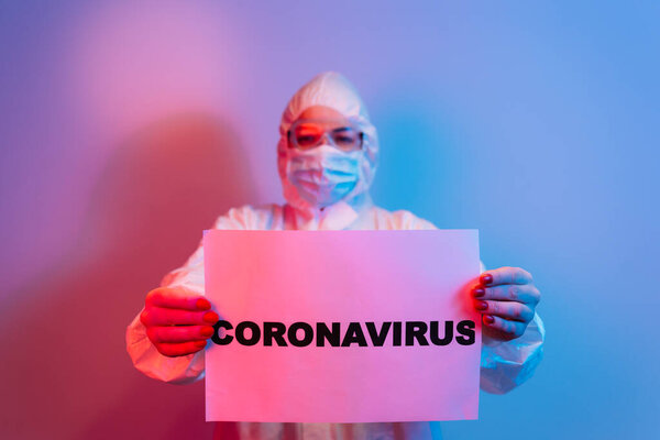 Коронавирус и карантин концепция. Профессиональный врач в защитном костюме, очках и маске для лица, держась за руки впереди, стоя изолированно на синем фоне
