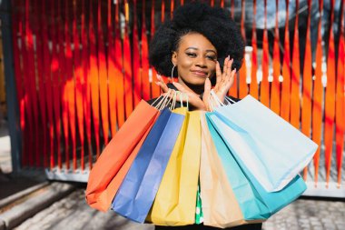 Dışarıda alışveriş torbalarıyla gülümseyen güzel siyah bir kadının portresi.