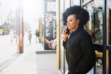 Neşeli Afrikalı kadın dışarıda akıllı telefon kullanıyor.