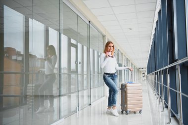 Havalimanı terminalinin girişindeki panoyu kontrol eden şık giyinmiş genç bir bayan yolcu. Uçuş çizelgesi arka planda maviye boyandı. Kadına odaklan..