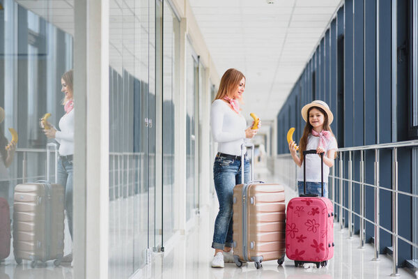 Woman with little girl in international airport. Mother with baby waiting for their flight. daughter with her mother eating bananas. Travelling with kids