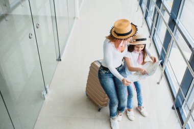 Anne ve küçük kızı havaalanı terminalinde bavul ve haritayla tatile hazırlar..