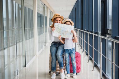 Anne ve küçük kızı havaalanı terminalinde bavul ve haritayla tatile hazırlar..