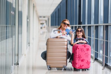 Havaalanı terminalinde bavul, biniş kartı ve pasaportu olan anne ve küçük kızı tatile hazır. Yüksek mevsim ve tatil konsepti. Rahatlayın ve yaşam tarzları