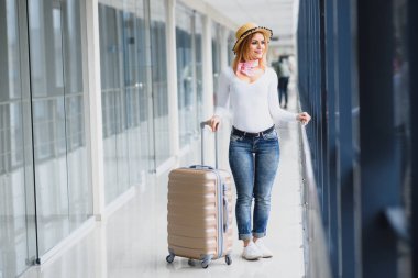 Gündelik giysiler giyen genç bir kadın havaalanında poz veriyor, çanta tutuyor ve kalkış pistinde bagajın yanında bekliyor..