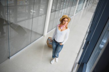 Gündelik giysiler giyen genç bir kadın havaalanında poz veriyor, çanta tutuyor ve kalkış pistinde bagajın yanında bekliyor..