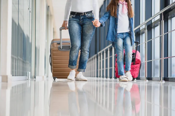 スーツケースを持ちながら空港ターミナルを歩いている幸せな若い母親と娘 ハイシーズンと休暇のコンセプト リラックスしてライフスタイル — ストック写真