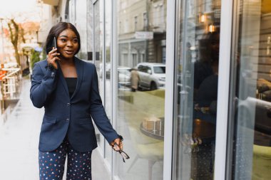 Endişeli yönetici dışarıda cep telefonuyla konuşuyor. Açık hava cam duvarının yanında duran genç Afrikalı Amerikalı iş kadını. Cep telefonu konuşma konsepti
