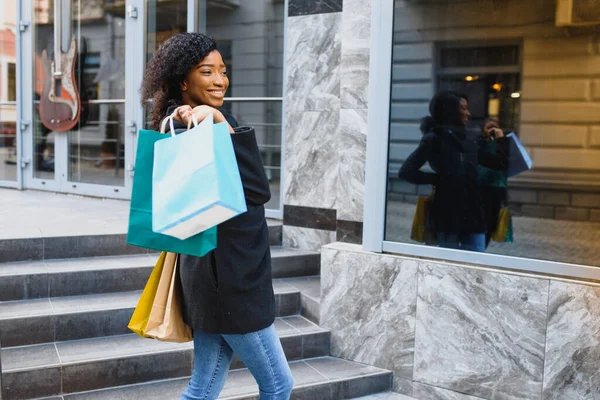 美丽的卷发非洲裔美国女人站在一家购物中心 手里拿着彩色购物袋 — 图库照片