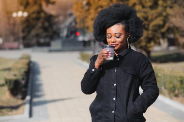 Güneşli bir günde, saçı örgülü ve sokakta yürüyen gülümseyen Afro-Amerikan bir kızın portresi. Açık hava fotoğrafı.