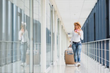 Havaalanında elinde bavulla gezen bir kız. Turist konsepti. Kadın havaalanı terminalinde bavuluyla yürüyor. seyahat kavramı