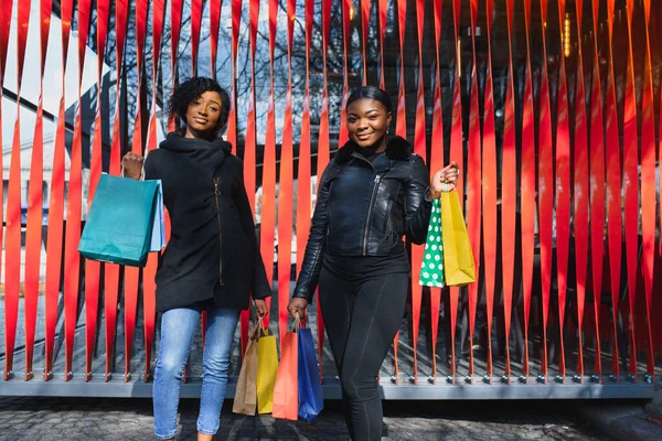 Two women friends in the city on a shopping trip carrying colorful shopping bags.
