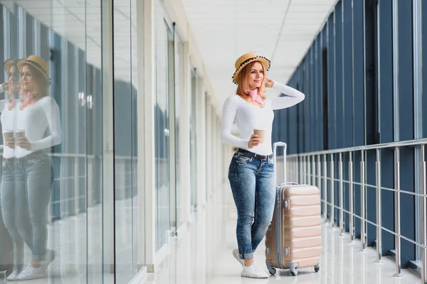 Young pretty stylish woman with luggage at the international airport. Waiting her flight at tax free shopping zone.