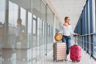 Havalimanı terminalinin girişindeki panoyu kontrol eden şık giyinmiş genç bir bayan yolcu. Uçuş çizelgesi arka planda maviye boyandı. Kadına odaklan..