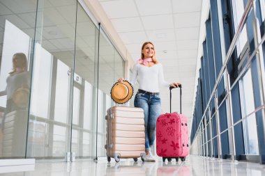 Havaalanı terminalinde bavuluyla yürüyen bir kadın, seyahat konsepti. Yüksek mevsim ve tatil konsepti. Rahatla ve yaşam tarzını değiştir. Seyahat ve Tatil Konsepti.