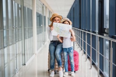 Anne ve küçük kızı havaalanı terminalinde bavul ve haritayla tatile hazırlar..