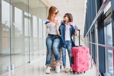 Havaalanı terminalinde bavul, biniş kartı ve pasaportu olan anne ve küçük kızı tatile hazır. Yüksek mevsim ve tatil konsepti. Rahatlayın ve yaşam tarzları