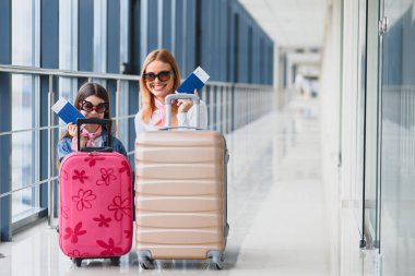 Havaalanı terminalinde bavul, biniş kartı ve pasaportu olan anne ve küçük kızı tatile hazır. Yüksek mevsim ve tatil konsepti. Rahatlayın ve yaşam tarzları