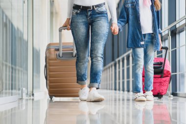 Mutlu genç anne ve kızı havaalanı terminalinde bir bavul taşırken yürüyorlar. Yüksek mevsim ve tatil konsepti. Rahatlayın ve yaşam tarzları