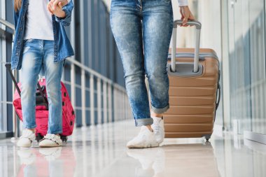 Mutlu genç anne ve kızı havaalanı terminalinde bir bavul taşırken yürüyorlar. Yüksek mevsim ve tatil konsepti. Rahatlayın ve yaşam tarzları